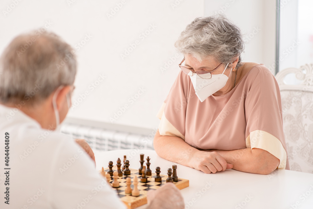 Senior woman and her husband wearing protective face masks play chess at home during quarantine Coronavirus (Covid-19) epidemic Senior woman and her husband wearing protective face masks play chess at home during quarantine Coronavirus (Covid-19) epidemic