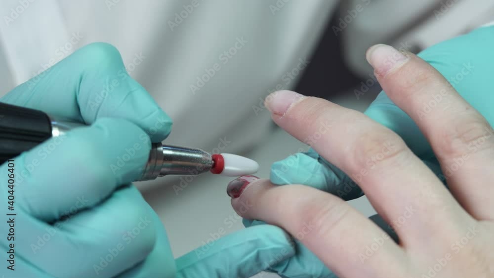 The master is removing the gel polish from the customer's nail with the help of a nail drill. Concept of the process of creating a professional manicure The master is removing the gel polish from the customer's nail with the help of a nail drill. Concept of the process of creating a professional manicure