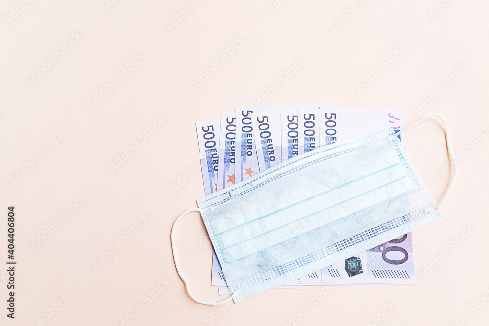 500 euro banknotes and a protective medical face mask on a light background. Health protection and financial well-being concept. 500 euro banknotes and a protective medical face mask on a light background. Health protection and financial well-being concept.