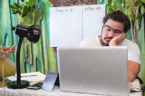 A freelance graphic designer working at home falls asleep while working on the laptop. A slightly unkempt man of mixed ancestry. photo