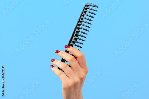 Female hand holding hair comb against blue background