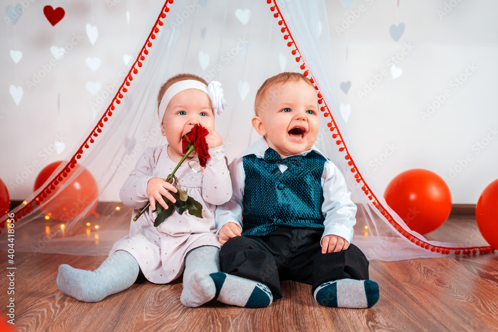 A couple of cute babies posing on a white background decorated with hearts. A happy girl eating a rose in her hands. Valentine's day
