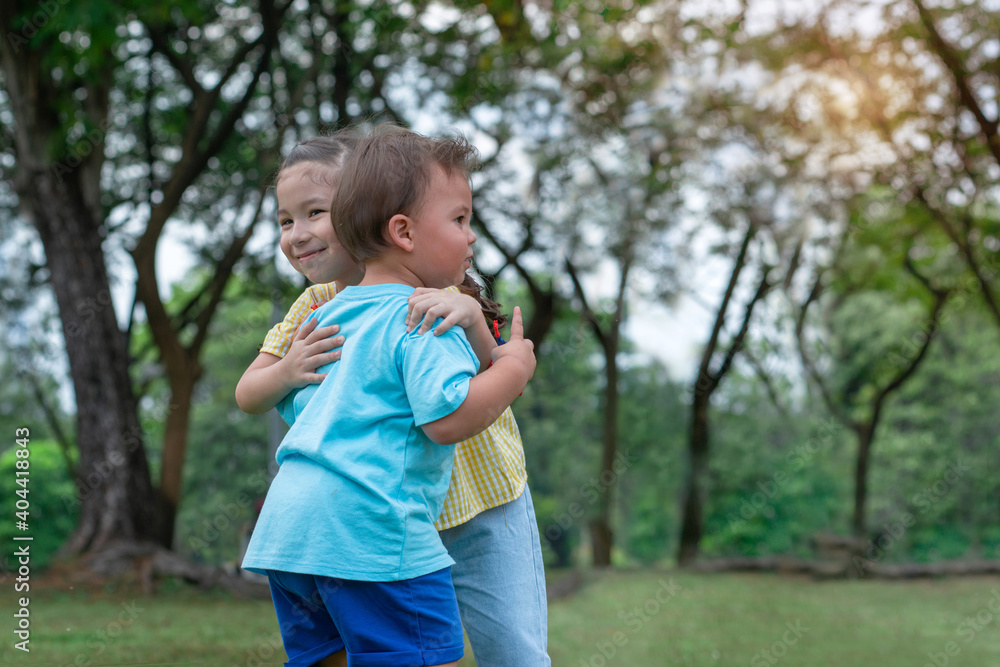 Sister hugging her brother on the green lawn in the summer, sibling love concept Sister hugging her brother on the green lawn in the summer, sibling love concept