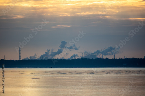 Smoke from chimneys of a metallurgical plant near a frozen lake