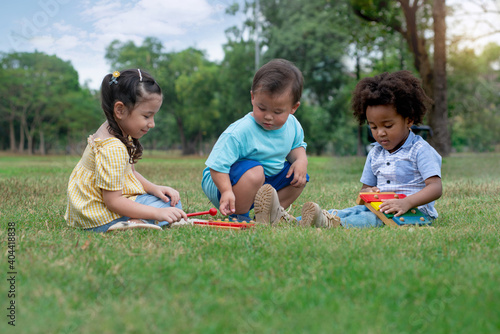 Three kids playing on lawn in the park on a summer day, group of diverse nation children playing together