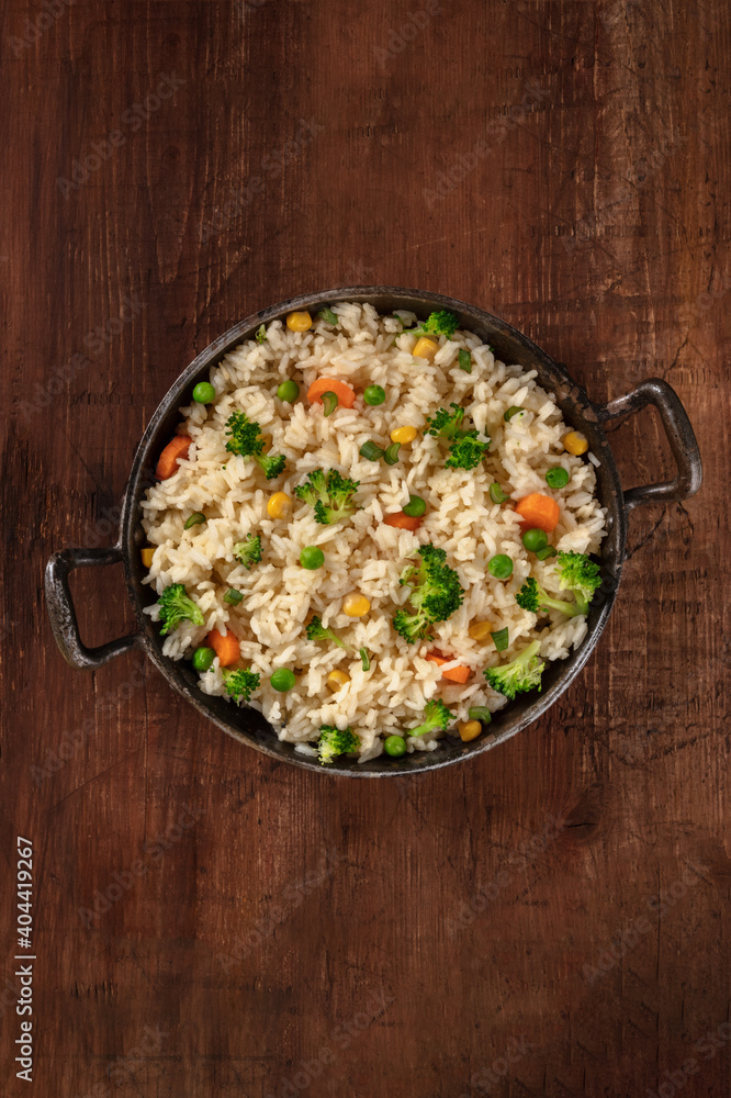 Vegan rice with broccoli, carrots and green peas, shot from above in a frying pan on a dark rustic wooden background, with a place for text Vegan rice with broccoli, carrots and green peas, shot from above in a frying pan on a dark rustic wooden background, with a place for text