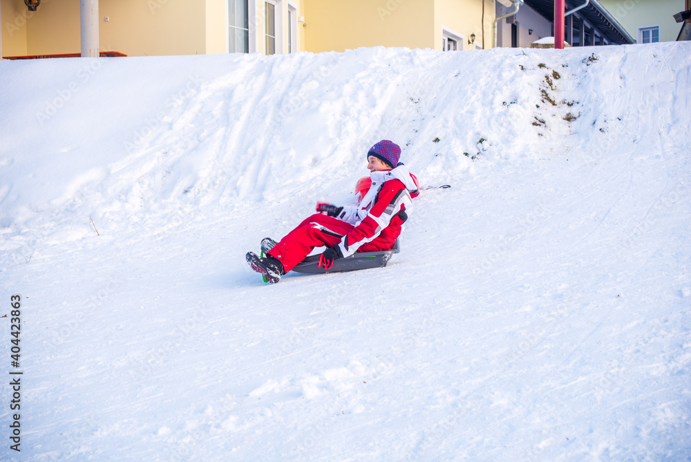Boy riding plastic sled downhill with houses in the background