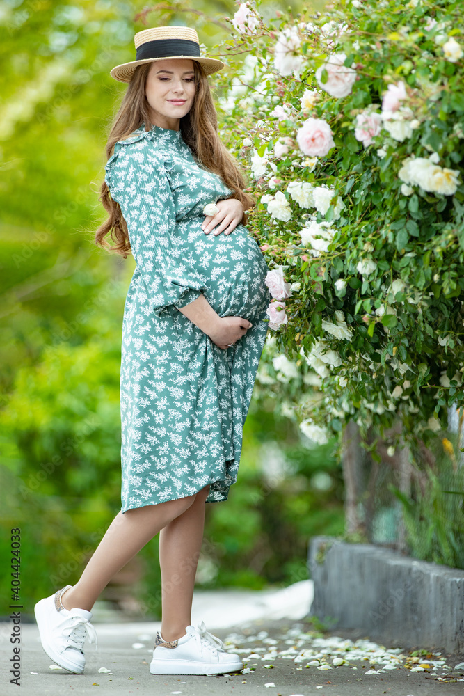 Beautiful young pregnant woman in nature with flowers. Pregnant girl with roses. High quality photo.