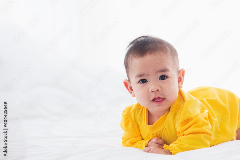 Portrait of beautiful young Asian newborn little baby prone on the bed at home, Happy baby smile wears a yellow shirt relaxing in the room, Family morning at home Portrait of beautiful young Asian newborn little baby prone on the bed at home, Happy baby smile wears a yellow shirt relaxing in the room, Family morning at home