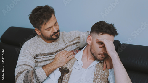 Portrait of two handsome men having trouble in relationship sitting on the couch and hugging. High quality photo