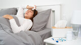 pill and glasses of water on the table woman suffering headache, fever and flu lying in bed background.