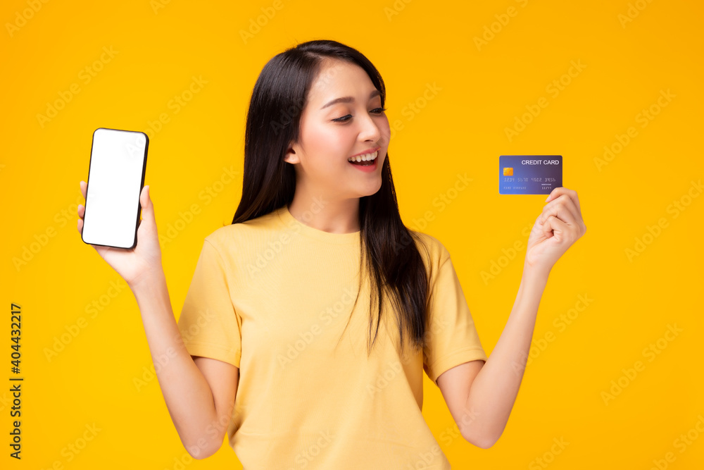Happy young woman holding smart phone and credit card and look at credit card with satisfied smile face. Use for your advertising Yellow background Internet banking and online shopping concept Happy young woman holding smart phone and credit card and look at credit card with satisfied smile face. Use for your advertising Yellow background Internet banking and online shopping concept