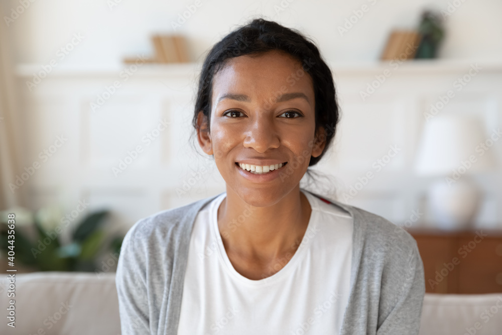 Head shot portrait of smiling attractive young african american multiracial woman sitting on sofa. Happy millennial biracial lady looking at camera, showing perfect whitening toothy smile indoors. Head shot portrait of smiling attractive young african american multiracial woman sitting on sofa. Happy millennial biracial lady looking at camera, showing perfect whitening toothy smile indoors.