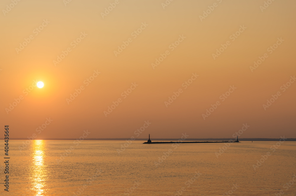A lighthouse against the sunset sky. Beautiful peaceful seascape. Small ships on the sea horizon.