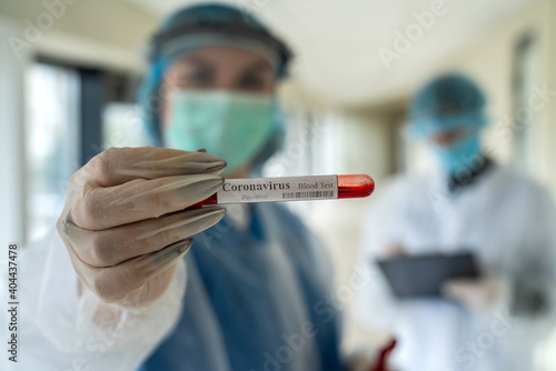 Two female doctors with protective clothes holds test tube with blood sample to coronavirus