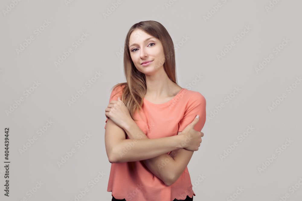 Fototapeta premium Portrait of gentle lovely beautiful young woman with blonde straight hair hugging herself, expresses self love and care