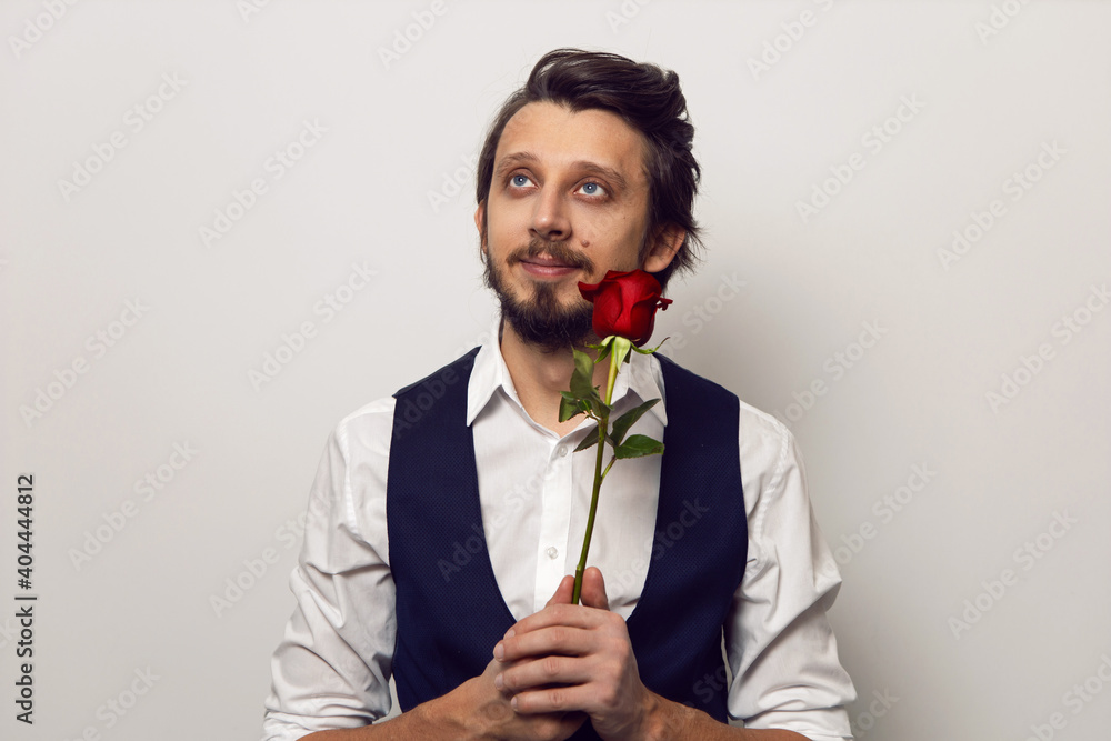 businessman man with a beard and glasses on Valentine's day in a white shirt and vest on a white background stands with a red rose businessman man with a beard and glasses on Valentine's day in a white shirt and vest on a white background stands with a red rose