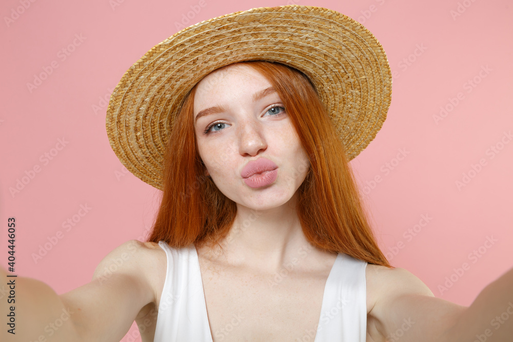 Young smiling cute cheerful caucasian pretty nice redhead woman 20s ginger long hair wear straw hat summer clothes doing selfie shot on mobile phone isolated on pastel pink background studio portrait. Young smiling cute cheerful caucasian pretty nice redhead woman 20s ginger long hair wear straw hat summer clothes doing selfie shot on mobile phone isolated on pastel pink background studio portrait.