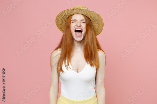 Young irritated angry hysteric stressed redhead woman 20s ginger long hair wearing straw hat summer clothes closed eyes screaming shouting isolated on pastel pink color background studio portrait