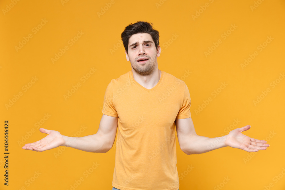 Young indignant troubled confused unshaved caucasian handsome man 20s in casual basic blank print design t-shirt spreading hands looking camera isolated on yellow color background studio portrait Young indignant troubled confused unshaved caucasian handsome man 20s in casual basic blank print design t-shirt spreading hands looking camera isolated on yellow color background studio portrait