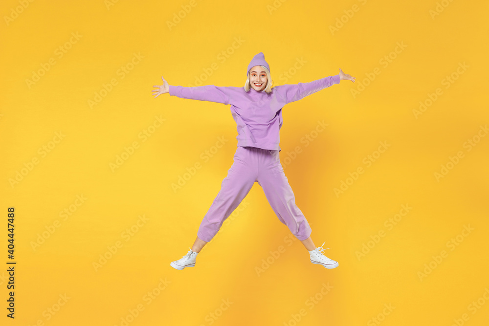 Full length of young overjoyed caucasian excited fun woman 20s bob haircut in casual basic purple suit beanie hat high jumping up with speading hands isolated on yellow background studio portrait.