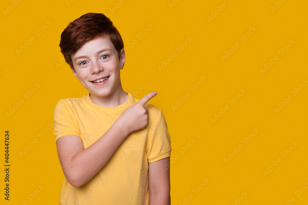 Caucasian ginger boy is advertising something pointing at the yellow studio free space Caucasian ginger boy is advertising something pointing at the yellow studio free space