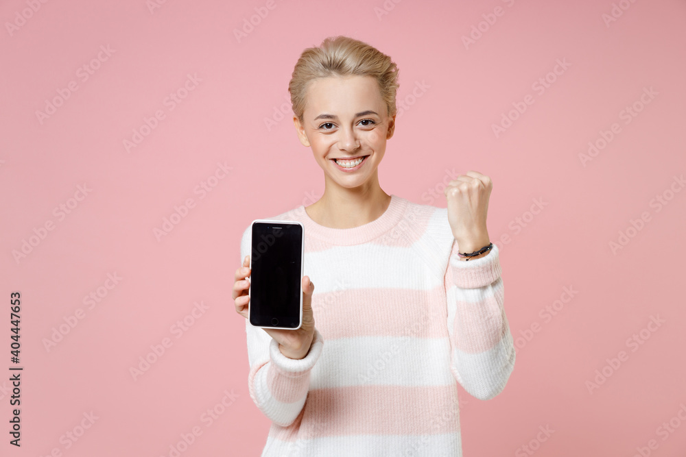 Young satisfied woman short haircut in sweater dental braces hold point finger on mobile phone blank screen copy space mock up doing winner gesture isolated on pastel pink background studio portrait. Young satisfied woman short haircut in sweater dental braces hold point finger on mobile phone blank screen copy space mock up doing winner gesture isolated on pastel pink background studio portrait.