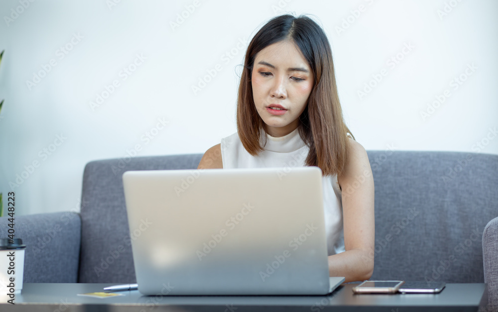 Asian young woman working on laptop computer while sitting at the living room, drinking coffee,work from home concept Asian young woman working on laptop computer while sitting at the living room, drinking coffee,work from home concept