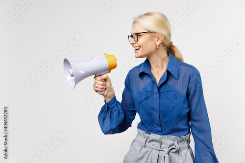 Blonde business woman in blue classic shirt glasses formal clothes scream in megaphone announces discounts sale hurry up look aside isolated on white background studio portrait. Communication concept