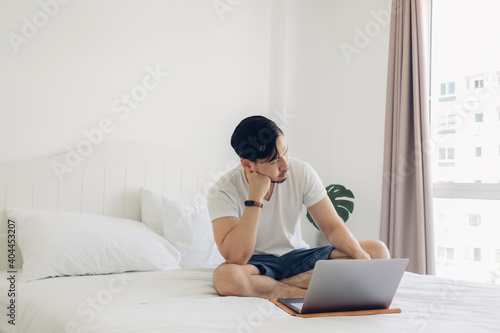 Asian man is sitting on the bed and working on his laptop.