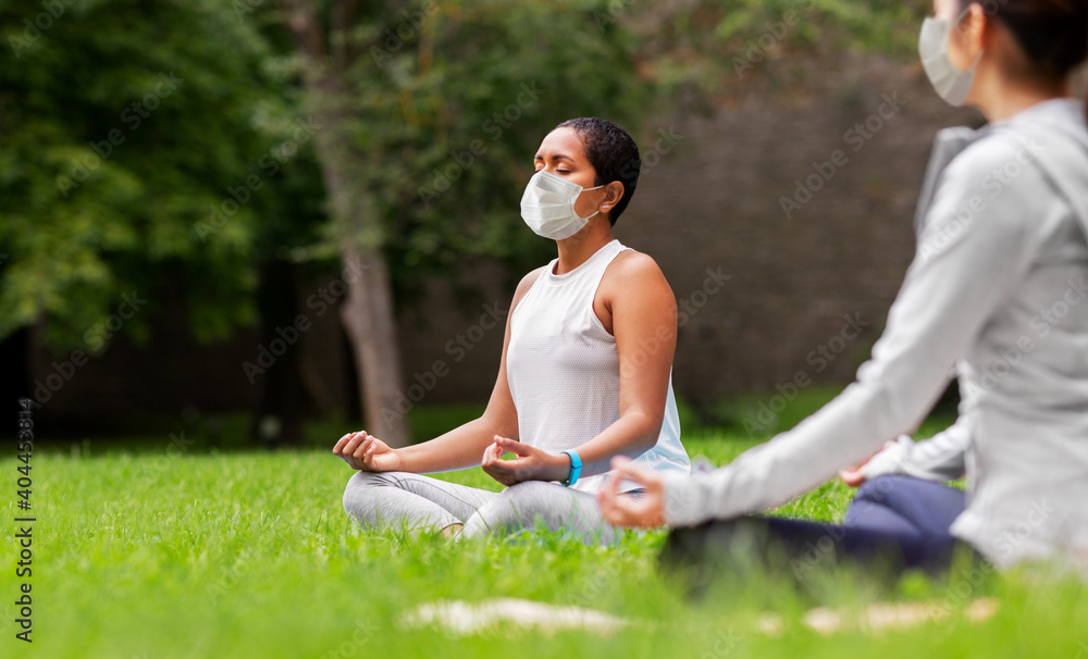 fitness, sport, yoga and healthy lifestyle concept - group of people wearing face protective medical mask for protection from virus disease meditating in lotus pose at summer park