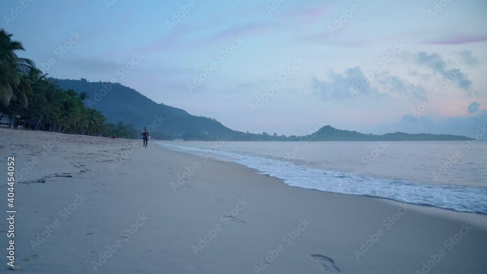 Athletic man in black sportswear running along the beach in the early morning on a tropical island Athletic man in black sportswear running along the beach in the early morning on a tropical island