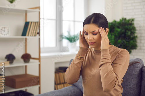 Obraz na płótnie Stressed woman sitting in chair in living-room or office, touching head with gri