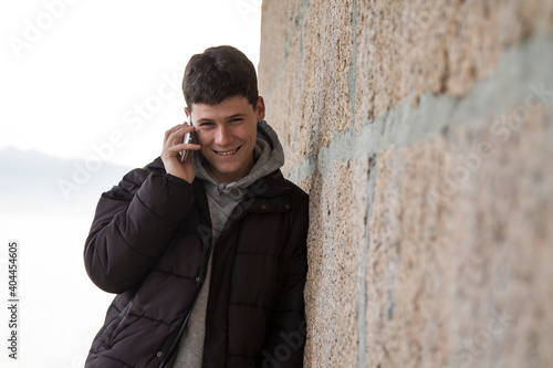 smiling man using smart phone on stone wall