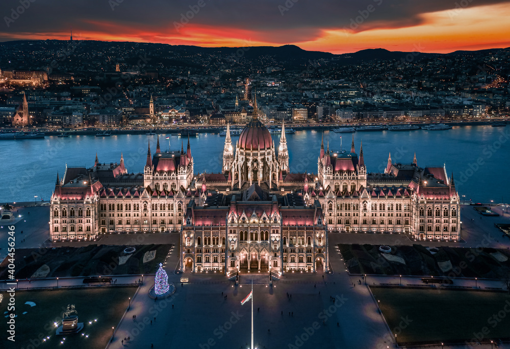 Budapest, Hungary - Aerial panoramic view of the beautiful illuminated Hungarian Parliament building at blue hour with Christmas tree. Buda Hills and River Danube at background on a December evening - obrazy, fototapety, plakaty 