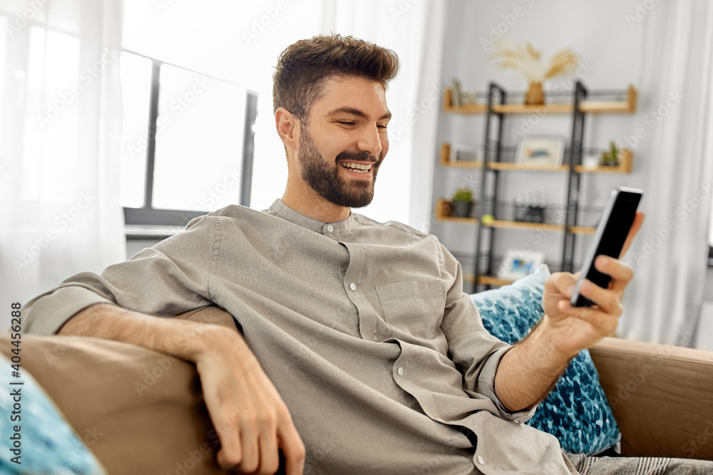 technology, internet, communication and people concept - happy smiling young man texting on smartphone at home technology, internet, communication and people concept - happy smiling young man texting on smartphone at home