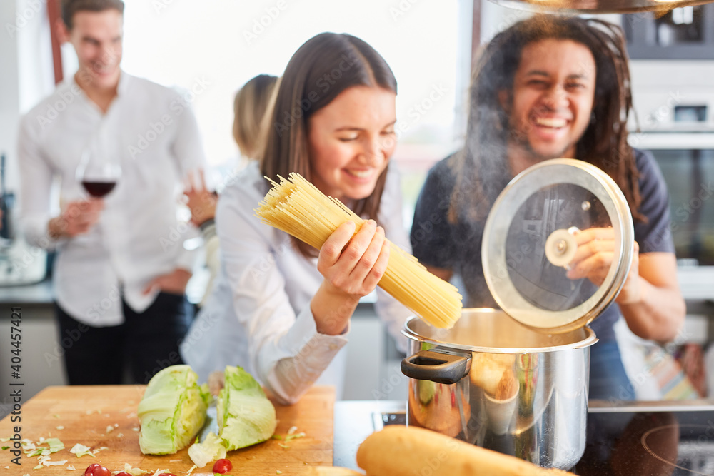 © Robert Kneschke - Lachende Freunde am Herd in Küche beim Nudeln kochen