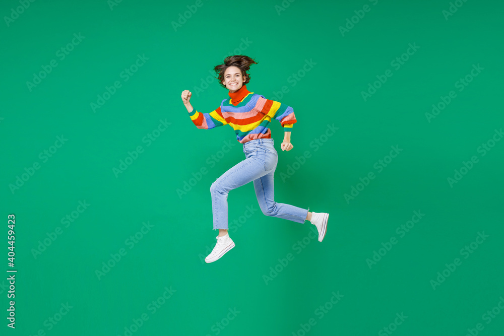 Full length side view of smiling laughing funny young brunette woman 20s years old wearing basic casual colorful sweater jumping like running isolated on bright green color background studio portrait.