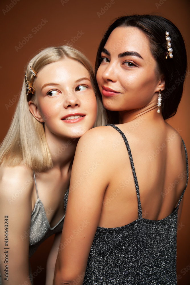 two pretty diverse girls happy posing together: blond and brunette on brown background, lifestyle people concept two pretty diverse girls happy posing together: blond and brunette on brown background, lifestyle people concept