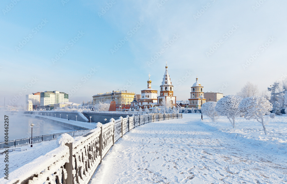 Siberian city of Irkutsk on winter day. View from snow-covered lower embankment of the Angara River to the Epiphany Cathedral and the monument to the founders of the city. Beautiful winter cityscape