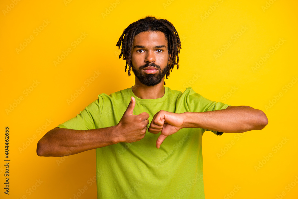 Photo of serious dark skin guy show thumb up thumb down symbol isolated over vivid yellow color background - obrazy, fototapety, plakaty 