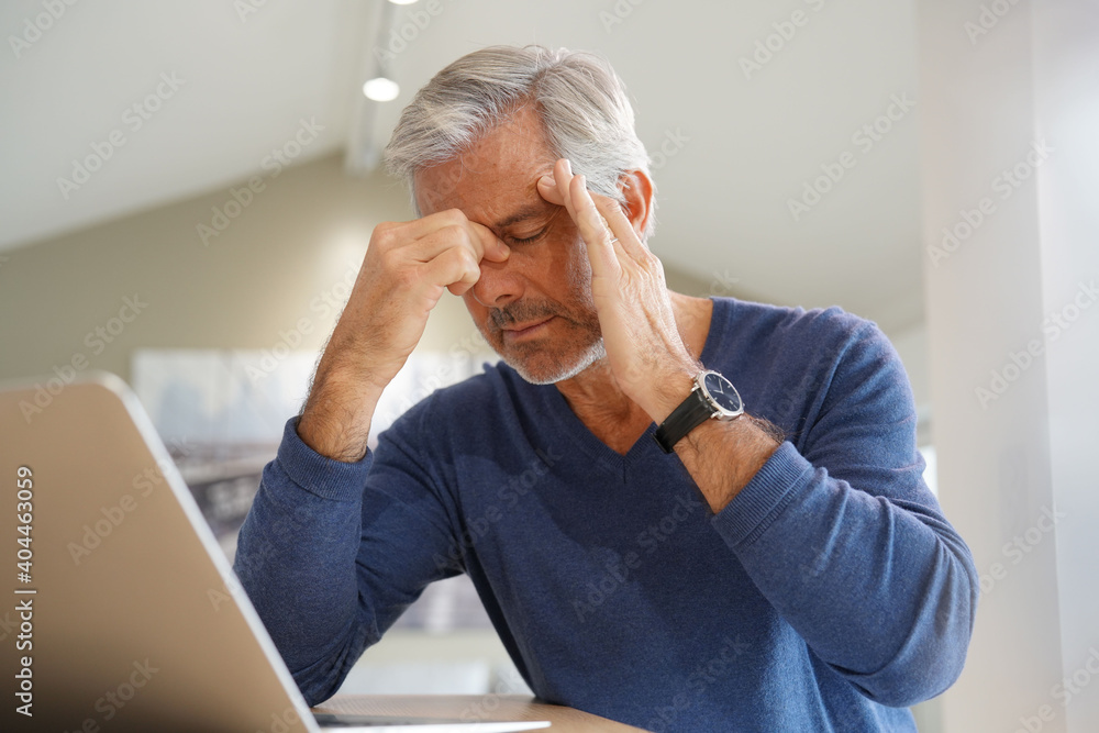 Senior man having a headache while working on laptop computer - obrazy, fototapety, plakaty 