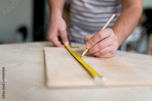 Close-up of man worker's hand measuring a wooden board with a ruler with scale