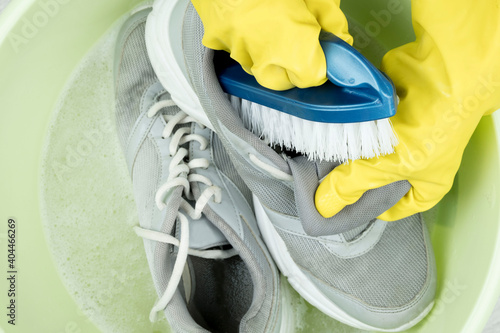 hands in rubber gloves clean sneakers with a brush. Brush and solution of water and detergent. Keep footwear fresh for its long-lasting run.