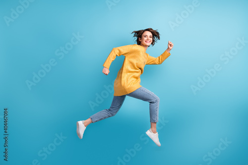 Full length body side profile photo of female runner smiling cherfully jumping high isolated on vivid blue color background