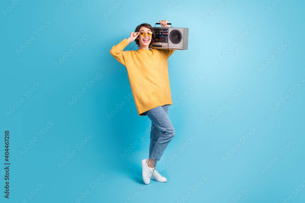 Full length body side profile photo of happy girl showing touching glasses keeping cassette recorder isolated on vivid blue color background Full length body side profile photo of happy girl showing touching glasses keeping cassette recorder isolated on vivid blue color background