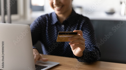 Close up view of happy woman sit at desk shopping online on computer with credit card. Smiling young female buyer pay on internet on laptop use secure banking service system app on gadget.
