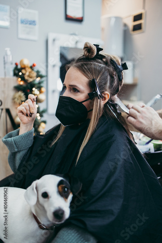 Hairdresser is dyeing female hair, making hair highlights to his client with a foil. She is wearing protective face mask as protection against virus pandemic.