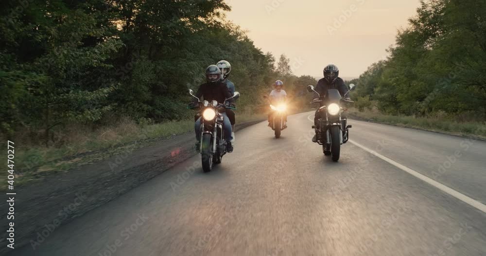 Bikers ride motorcycles with lights turned on, the road goes through the forest Bikers ride motorcycles with lights turned on, the road goes through the forest