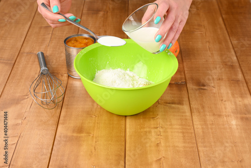 A woman pours milk into a tablespoon. Mixing ingredients for the pie.
